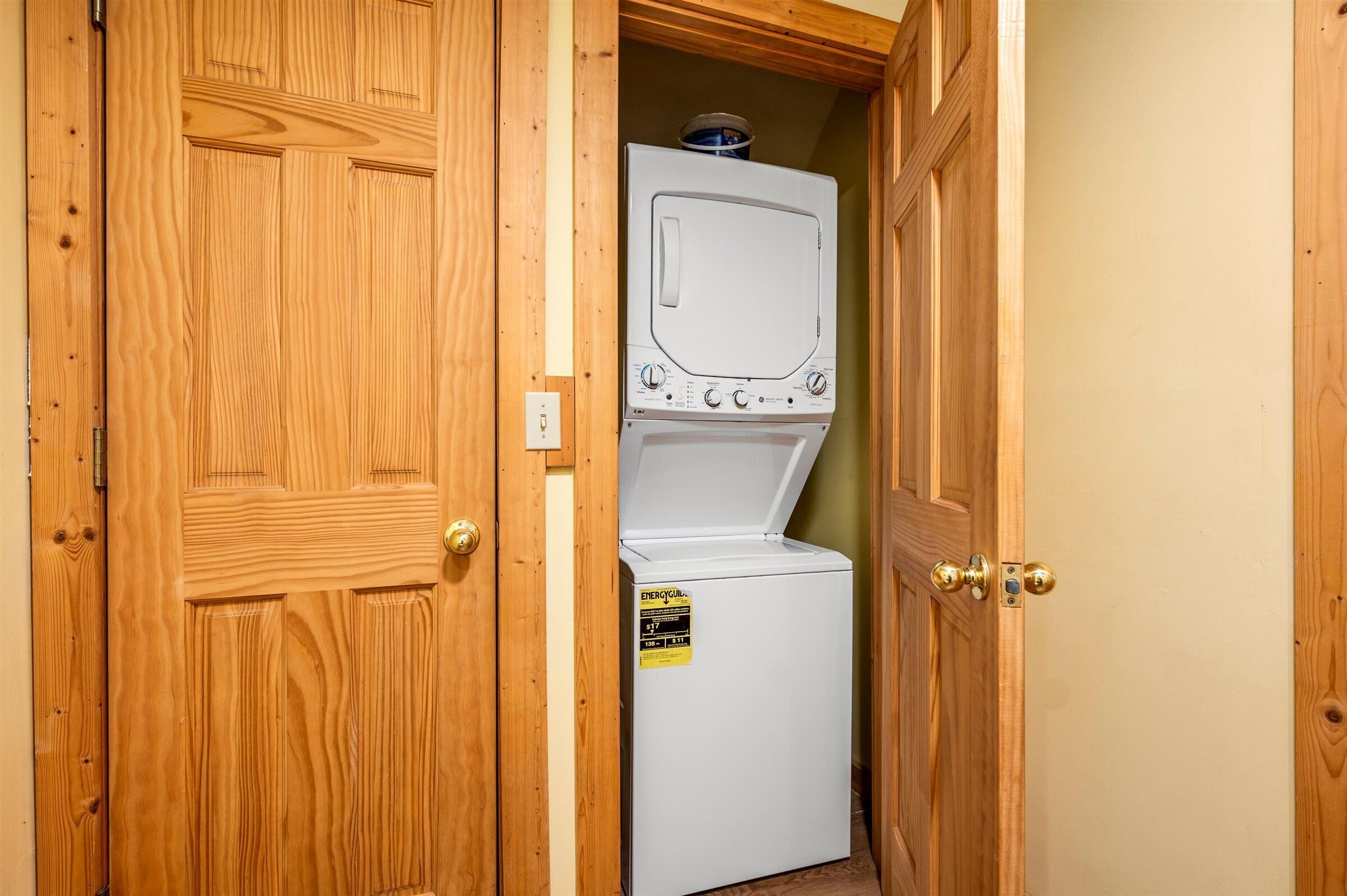 Une buanderie équipée d’un lave-linge et d’un sèche-linge à chargement frontal, de portes en bois et d’une étiquette d’efficacité énergétique bien visible.