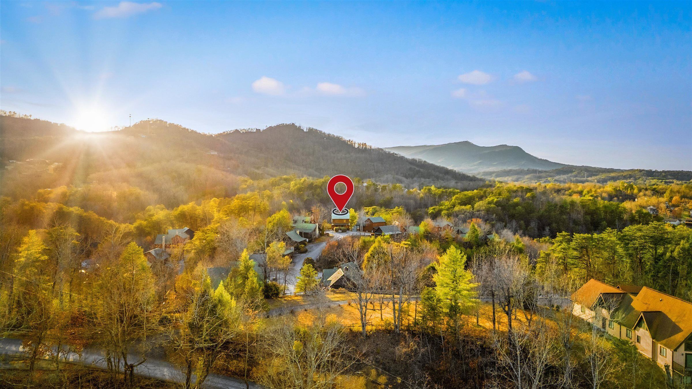 A rural village with houses surrounded by autumn foliage and mountains in the background.
