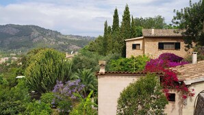 Una casa in pietra con tetto in tegole circondata da vegetazione lussureggiante e piante fiorite.