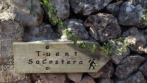 Un cartello di legno con la scritta 'Tuent Sacostera' e la sagoma di un escursionista, posto su uno sfondo roccioso.