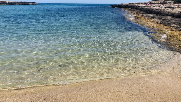 Una playa despejada con aguas tranquilas y un litoral rocoso.