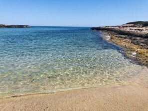 Une plage de sable fin aux eaux calmes et dont le rivage est rocheux.