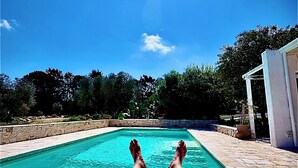 Una persona descansando junto a una piscina, con cielo azul despejado y vegetación al fondo.