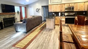 Uma sala de estar ampla com lareira, um sofá, uma mesa de jantar e piso de madeira.