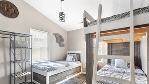 Quarto com duas beliches, uma estante de metal, um relógio e uma janela com persianas.