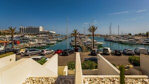 Un puerto deportivo con barcos, un hotel al fondo y coches aparcados.