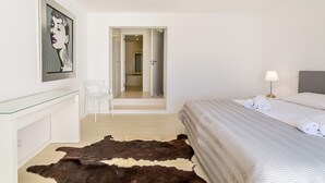 Habitación de hotel con cama, escritorio, silla, alfombra de cuero de vaca, un cuadro y un baño visible a través de una puerta abierta.