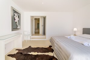 A hotel room with a bed, a desk, a chair, a cowhide rug, a painting, and a bathroom visible through an open door.