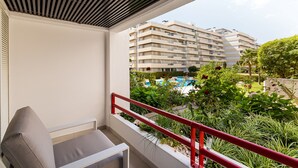 Un balcón con barandilla roja, una silla gris y vista a un edificio con varios balcones y una piscina.