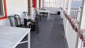 A covered outdoor area with tables and chairs, a fire extinguisher, and a view of a building in the background. - SunShine Motel (Wildwood)