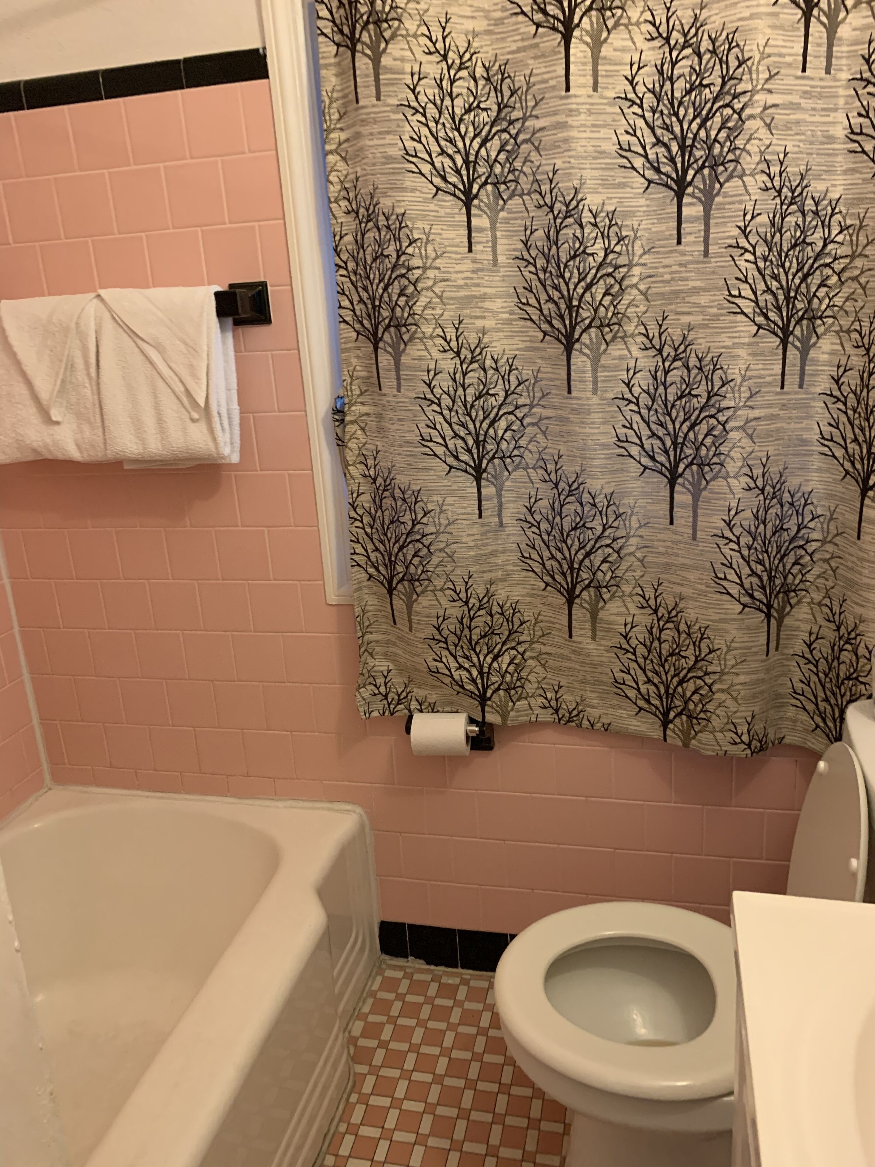 A bathroom with a tiled floor, a bathtub, a toilet, and a shower curtain with a tree pattern.