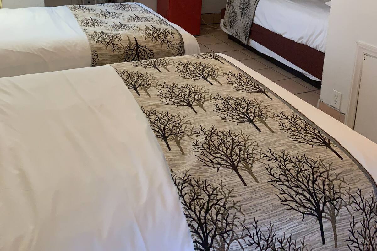A hotel room with two beds, a TV, a red microwave, and a window with curtains.