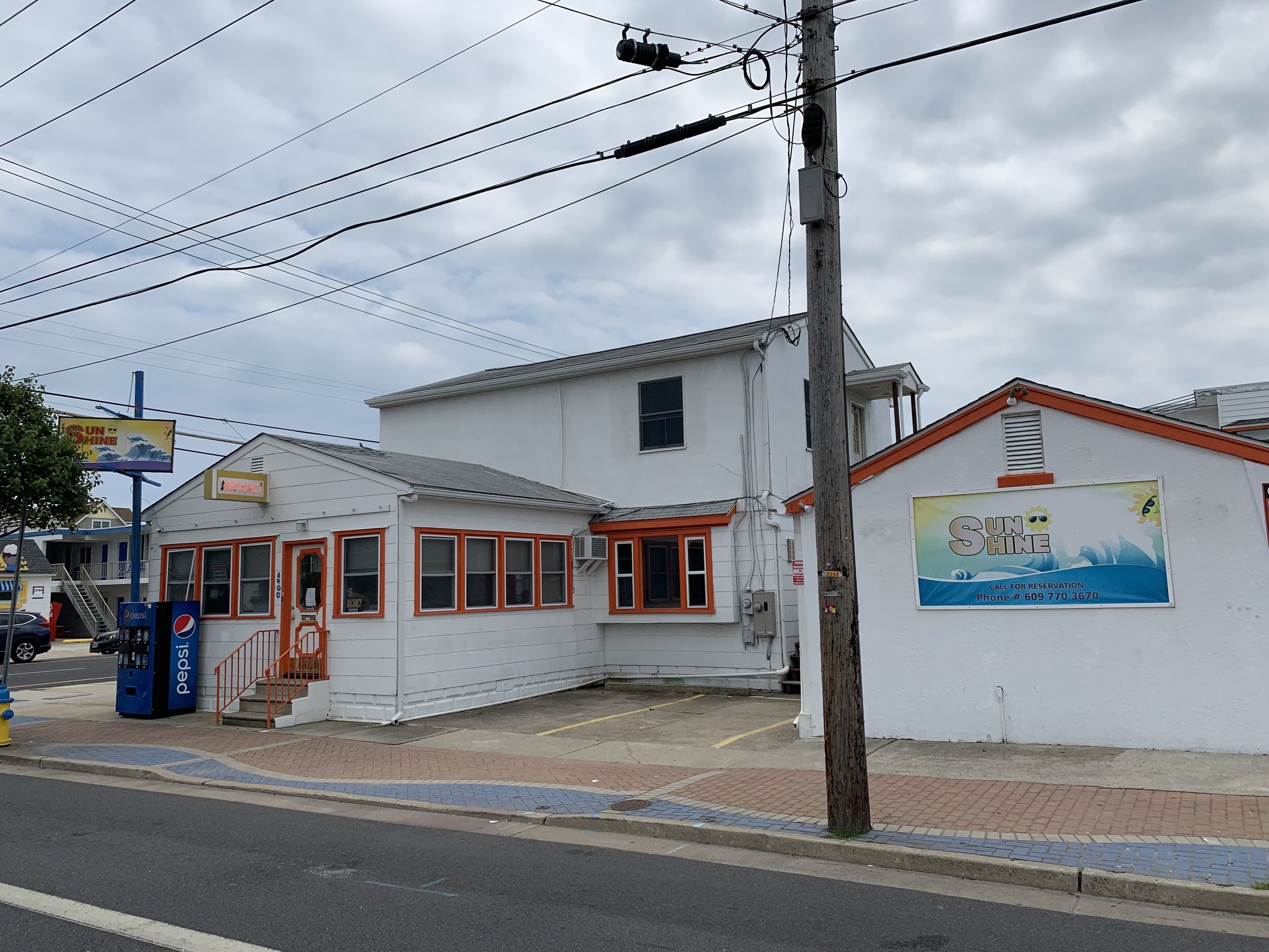 A white building with orange trim, a Pepsi vending machine, and a sign for 'Sunshine'.