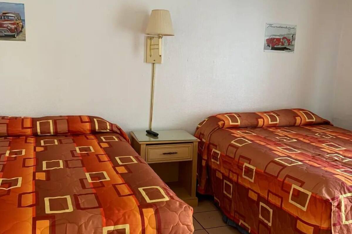 A hotel room with two beds, a ceiling fan, a nightstand with a lamp, and wall decorations.