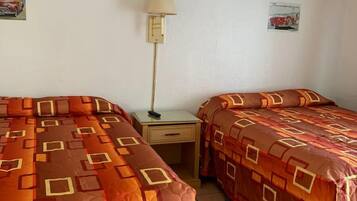 Een hotelkamer met twee bedden, een plafondventilator, een nachtkastje, een lamp en een poster aan de muur.