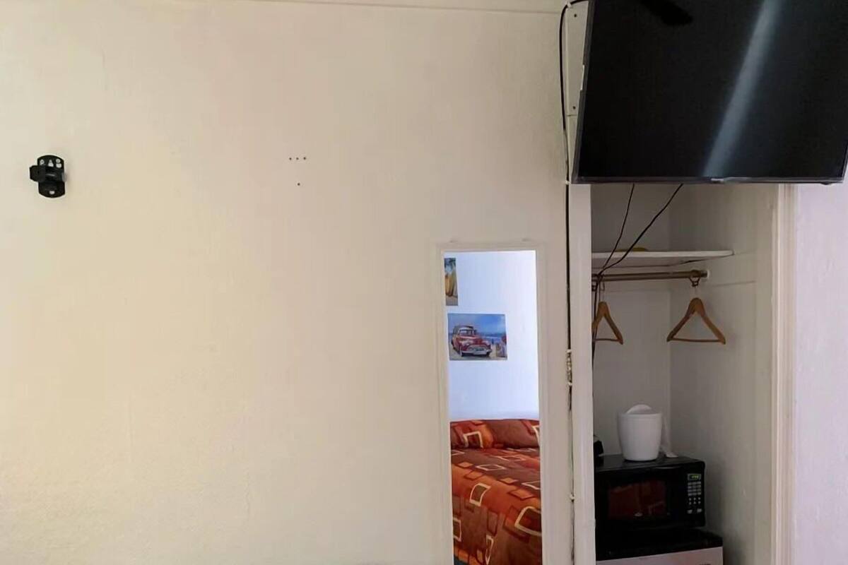 A room with a green sofa, a television mounted on the wall, a bed with a patterned bedspread, and a small refrigerator.