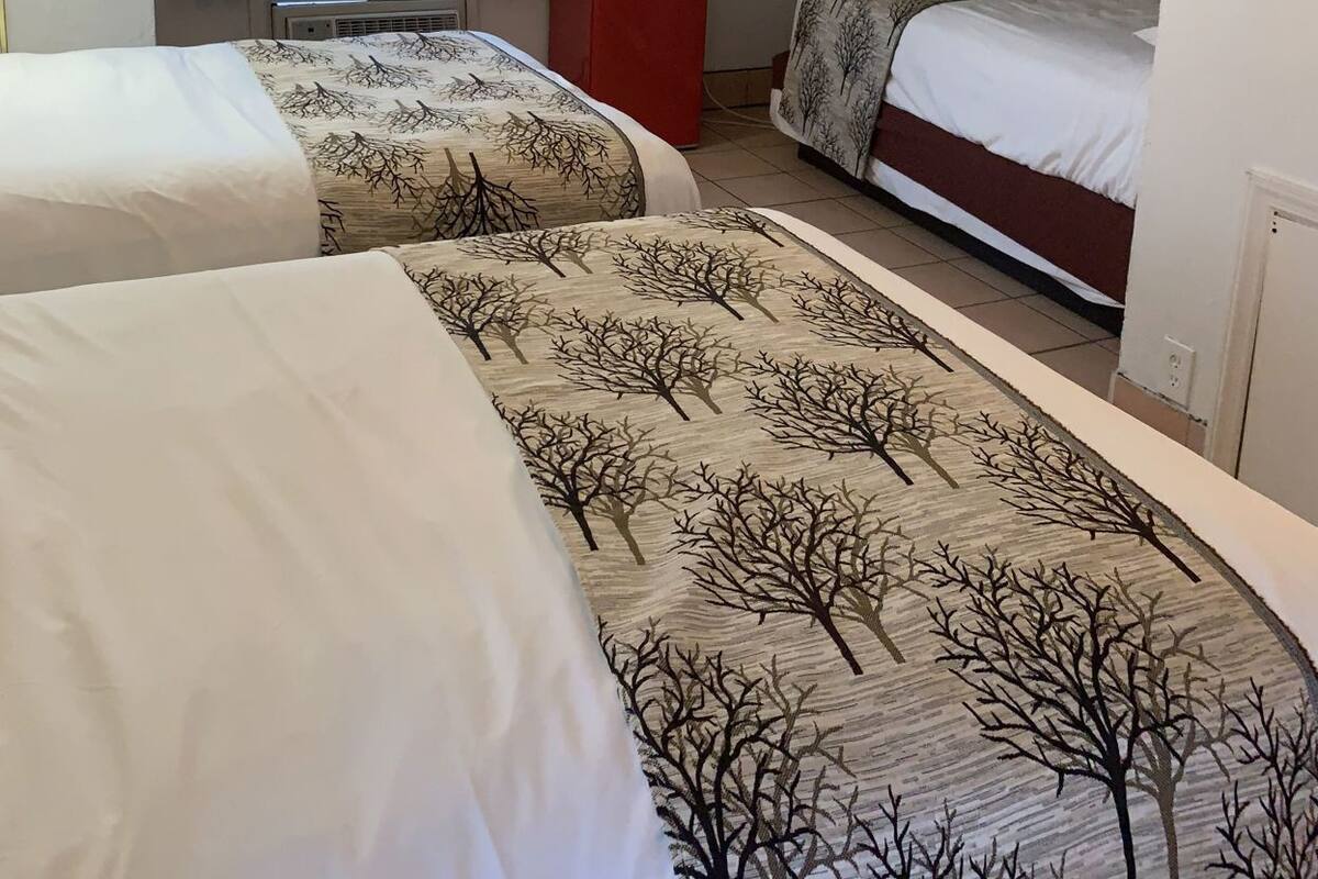 A hotel room with two beds, a TV, a red microwave, and a window with curtains.