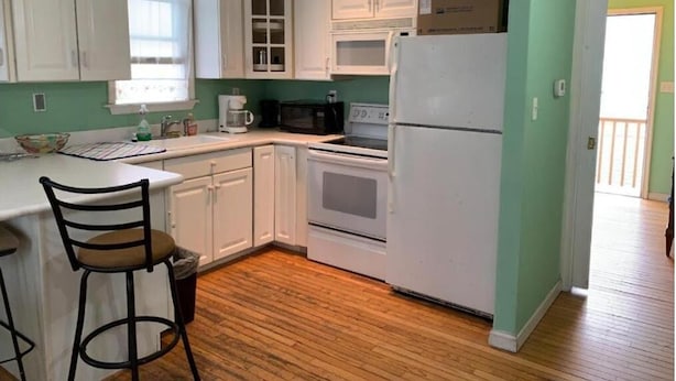 A kitchen with white cabinets, a microwave, a stove, and a refrigerator. - SunShine Motel (Wildwood)