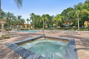 Uma área com hidromassagem, espreguiçadeiras, piscina e palmeiras.