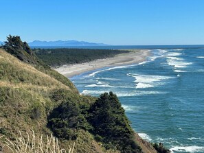 Paisagem costeira com praia, ondas do oceano e montanhas ao longe.