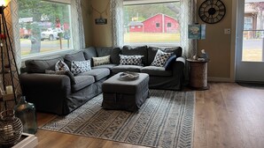 A living room with a sectional sofa, a coffee table, a rug, and a view of a red barn through large windows. - Beach Melody, Long Beach WA (Long Beach)