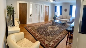 A modern living room with a large rug, a sofa, a coffee table, and a ceiling fan. - Historic Bungalow! 2bed, 2bath, 2den, Downtown Humble, IAH 8min! (Humble)