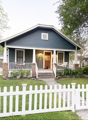 A two-story house with a front porch, a brick foundation, and a white picket fence. - Historic Bungalow! 2bed, 2bath, 2den, Downtown Humble, IAH 8min! (Humble)
