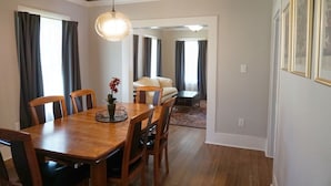 A dining area with a wooden table and chairs, a hanging light fixture, and a sofa in the background. - Historic Bungalow! 2bed, 2bath, 2den, Downtown Humble, IAH 8min! (Humble)