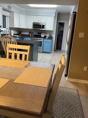 Eine moderne Küche mit weißen Schränken, Edelstahlgeräten und einem Esstisch aus Holz mit Platzdeckchen.