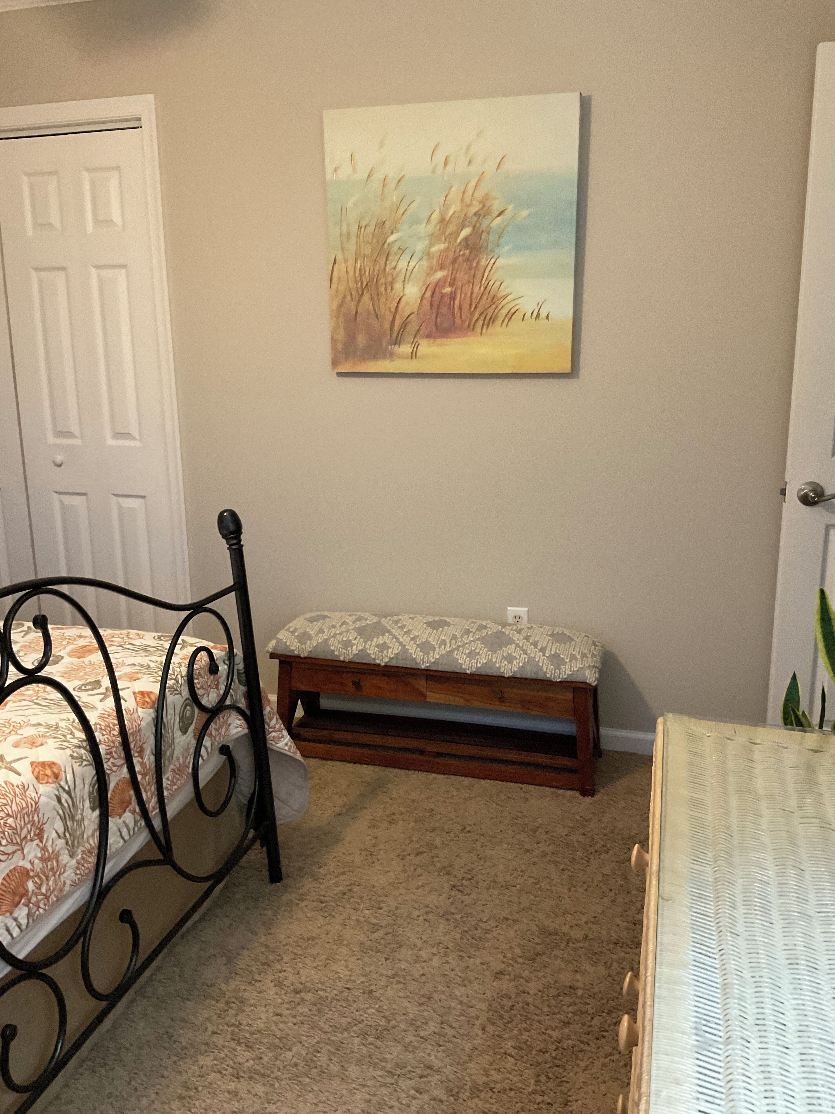 A bedroom with a bed, a bench, and a painting on the wall.