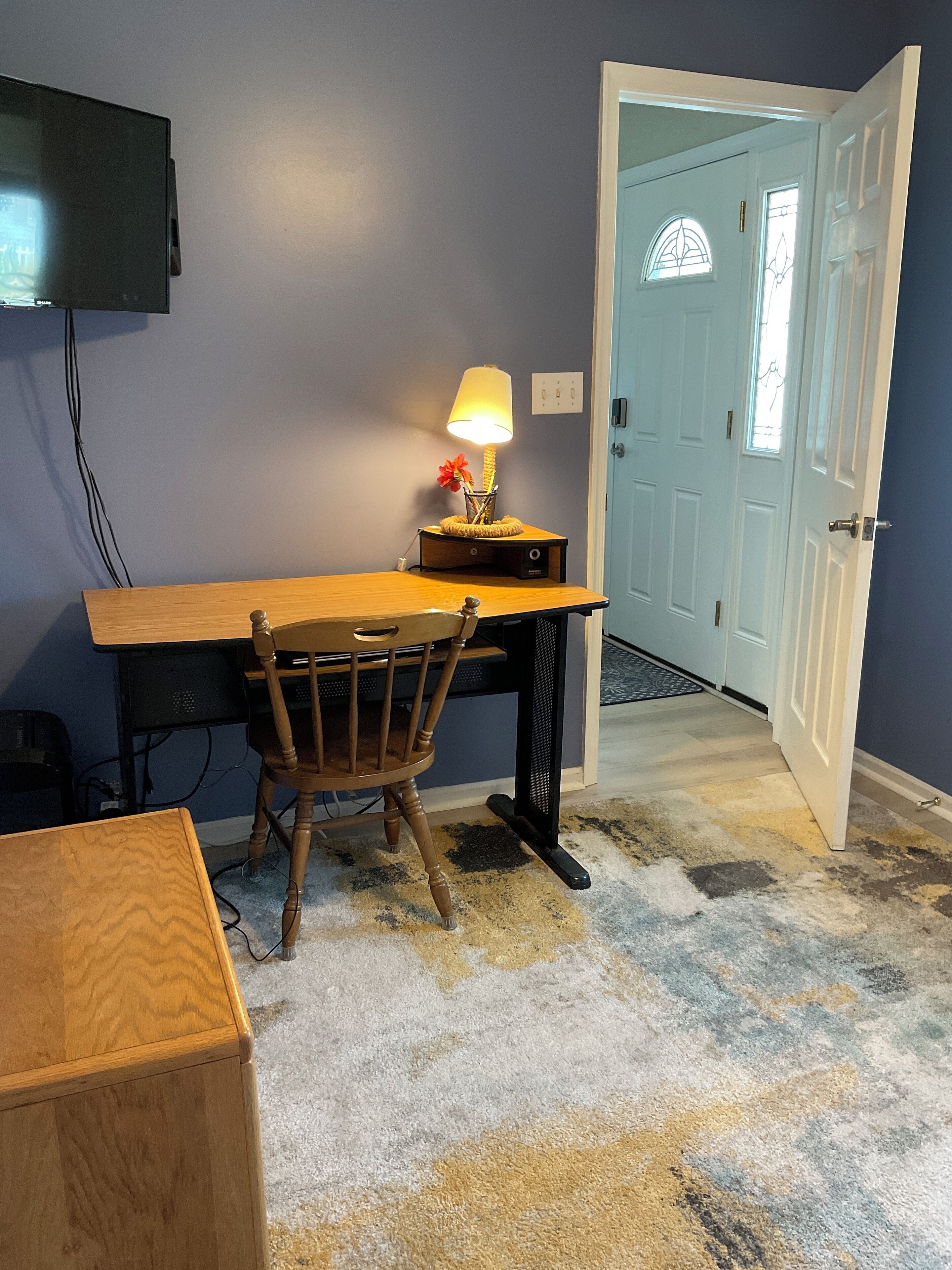 Um quarto com uma escrivaninha de madeira, uma cadeira, uma luminária e uma televisão na parede.