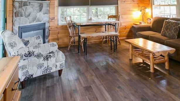 Interior acogedor de una cabaña con techo de madera, chimenea, mesa de comedor y sofá.