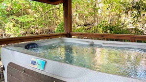 Un jacuzzi con panel de control digital, rodeado por una terraza de madera y abundante vegetación.