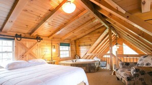 Un dormitorio acogedor en el ático con una cama grande, una zona de estar con una silla, un jacuzzi y un ventanal con vistas.