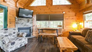Interior acogedor de una cabaña con chimenea de piedra, mesa de comedor de madera y televisor montado arriba.