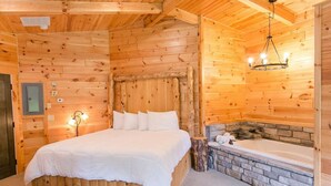 Un dormitorio de cabaña de madera con una cama, una chimenea de piedra y un candelabro.