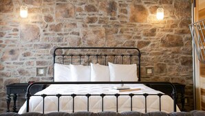 A bed with a metal frame and white bedding in a room with a stone wall. - Unique Rustic Suite with Jacuzzi Tub, Kitchen, Fireplace, and Living Room (Millersburg)
