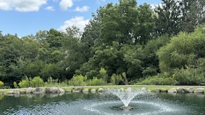 A tranquil pond with a central fountain, surrounded by lush greenery and a stone border. - Unique Rustic Suite with Jacuzzi Tub, Kitchen, Fireplace, and Living Room (Millersburg)