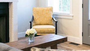 A living room with a yellow armchair, a fireplace, a coffee table with a vase of flowers, and a large window. - Unique Rustic Suite with Jacuzzi Tub, Kitchen, Fireplace, and Living Room (Millersburg)