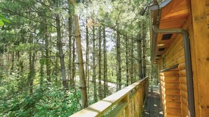 A wooden deck with a railing overlooking a dense forest. - Romantic Treehouse Getaway with Treetop Views (Millersburg)