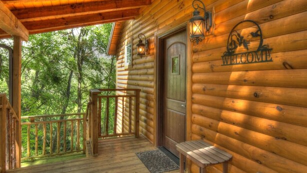A wooden cabin with a porch, a welcome sign, and a door. - Romantic Treehouse Getaway with Treetop Views (Millersburg)