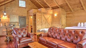 A log cabin interior with a large leather sofa, wooden dining table, and a kitchen area. - Romantic Treehouse Getaway with Treetop Views (Millersburg)