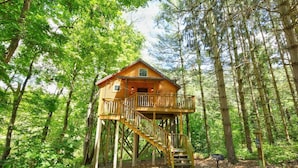 A wooden cabin with a balcony and stairs, surrounded by a forest. - Romantic Treehouse Getaway with Treetop Views (Millersburg)