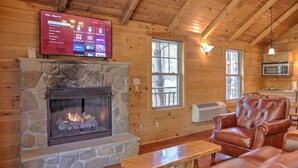 A cozy cabin interior with a stone fireplace, leather furniture, a mounted TV, and a wooden ceiling. - Romantic Treehouse Getaway with Treetop Views (Millersburg)