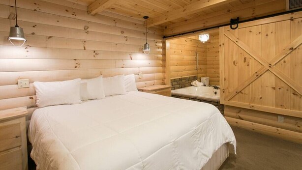 Un dormitorio de estilo cabaña de madera con una cama grande, un armario de madera y una bañera.
