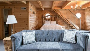 A log cabin interior with a bed, a staircase, and a grey upholstered sofa with patterned cushions. - Luxury Lodge Suite with Jacuzzi - Near Berlin Ohio (Berlin)