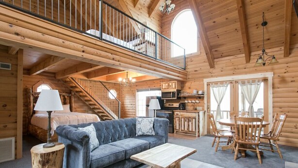 A log cabin interior with a sofa, dining table, chairs, a staircase, and a kitchen area. - Luxury Lodge Suite with Jacuzzi - Near Berlin Ohio (Berlin)