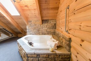 L’intérieur d’un chalet en bois, avec un mur en pierre, un plafond en bois et une baignoire blanche agrémentée de serviettes et d’une bouteille.