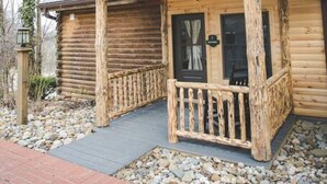 A log cabin with a wooden porch, a black door, and a stone pathway leading to the entrance. - Luxury Lodge Suite with Jacuzzi - Near Berlin Ohio (Berlin)