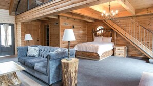 A log cabin interior with a loft bedroom, a sofa, a lamp, and a staircase. - Luxury Lodge Suite with Jacuzzi - Near Berlin Ohio (Berlin)